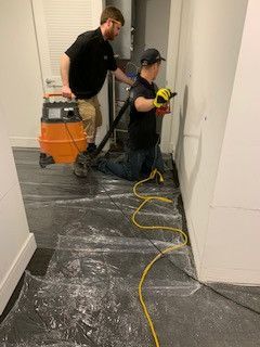 Two men are cleaning a room with a vacuum cleaner.