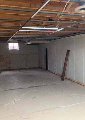 An empty basement with a ceiling fan and a window.