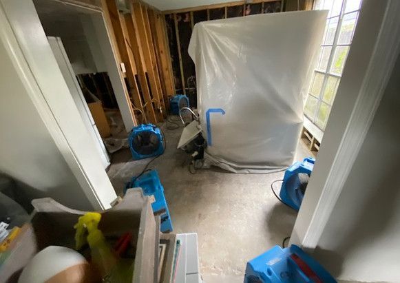 A room with a lot of cleaning supplies in it and a white tarp on the wall.
