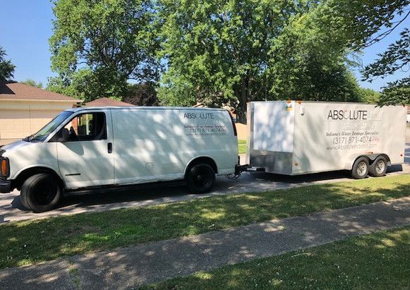 A white van with a trailer attached to it is parked on the side of the road.