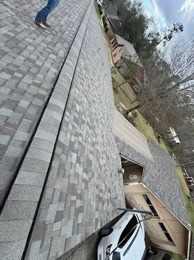Person on a shingled roof, looking down at a driveway and a white car parked in a garage.