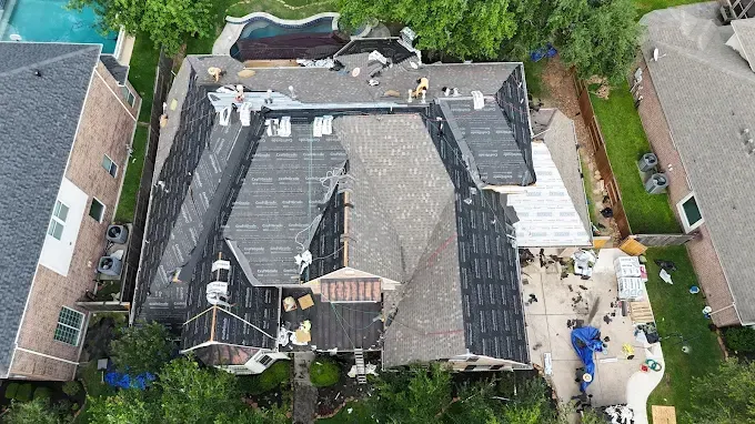 Aerial view of a house undergoing roof repair; workers are present.