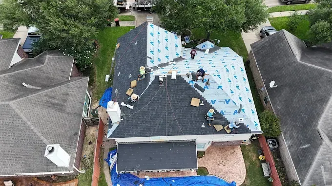 Roofers on a house roof. One section covered in blue tarp, others partially covered with new shingles.