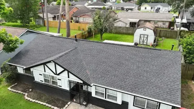 A house with a black roof and white and black trim, viewed from above. Green grass and other houses surround.