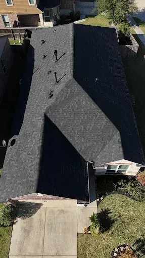 Overhead view of a house with a dark gray shingled roof, a concrete walkway, and some greenery.