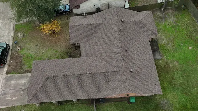 Overhead view of a house with a brown shingled roof, set on a green grassy lawn.