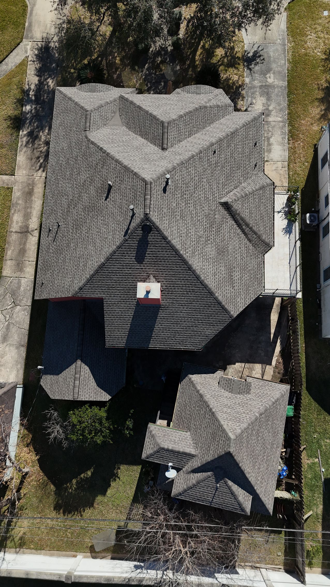 Overhead view of a house with a complex, multi-gabled roof, surrounded by lawn and a sidewalk.