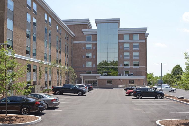 A parking lot in front of a large brick building with cars parked in front of it.