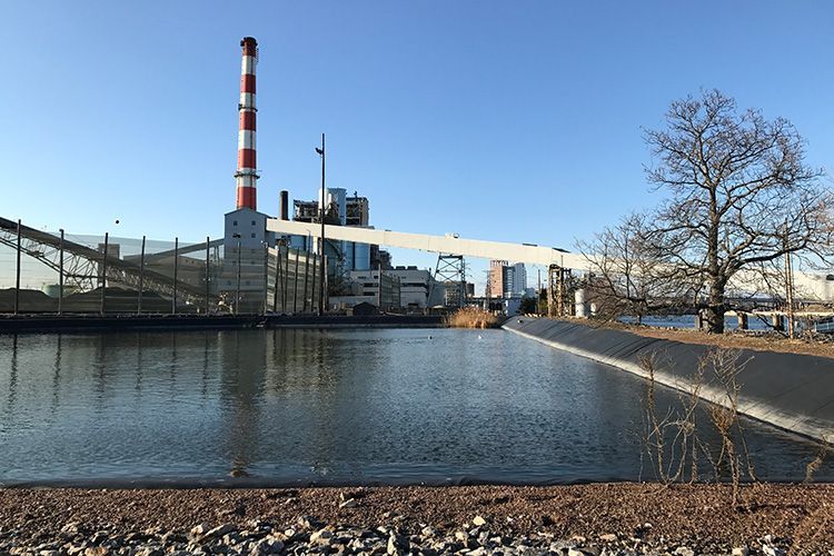 A large powerplant with a red and white chimney is next to a body of water.
