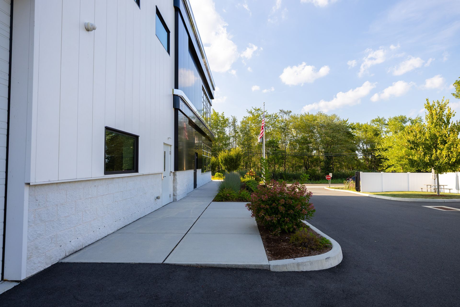 White building exterior, asphalt parking lot, sidewalk, landscaping, and blue sky.