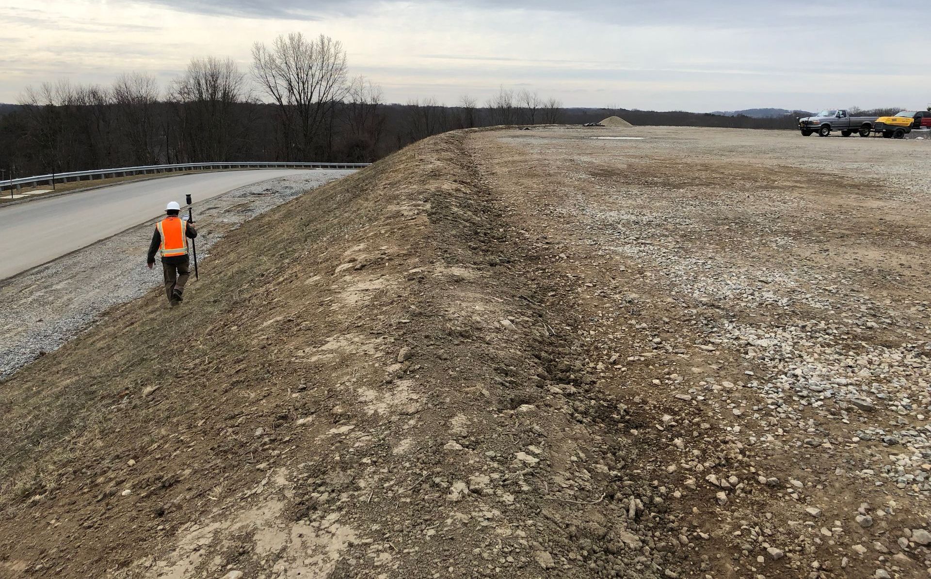 A man in an orange vest is walking down a dirt road.