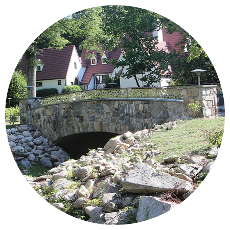 A stone bridge over a stream with a building in the background