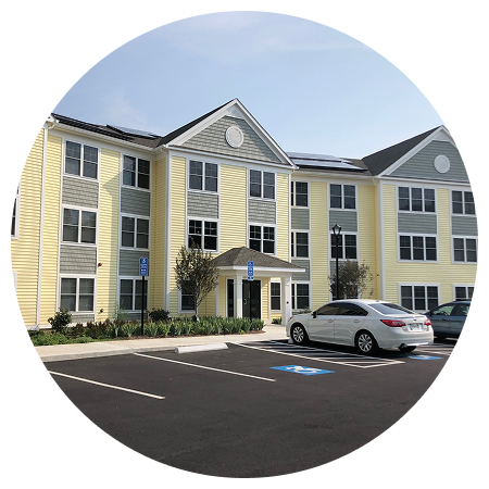 A white car is parked in front of a large apartment building.