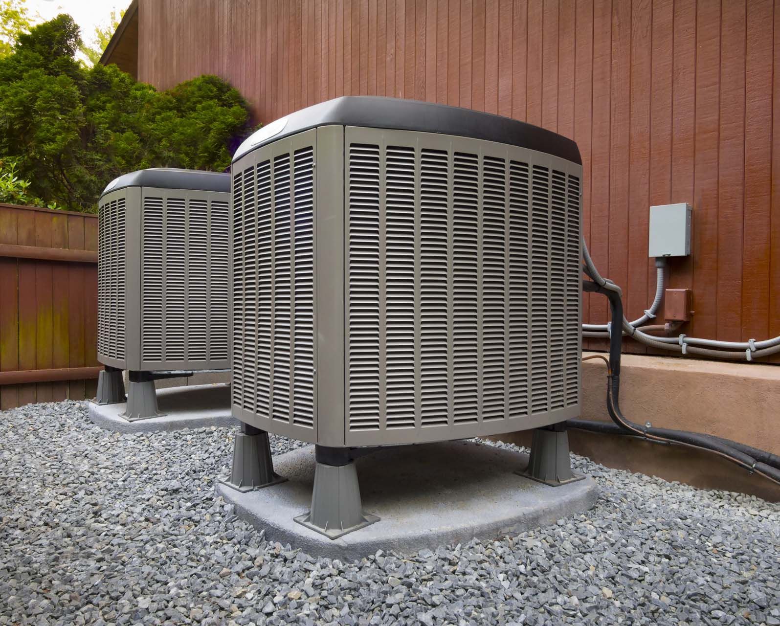 Two air conditioners are sitting on top of gravel outside of a building.