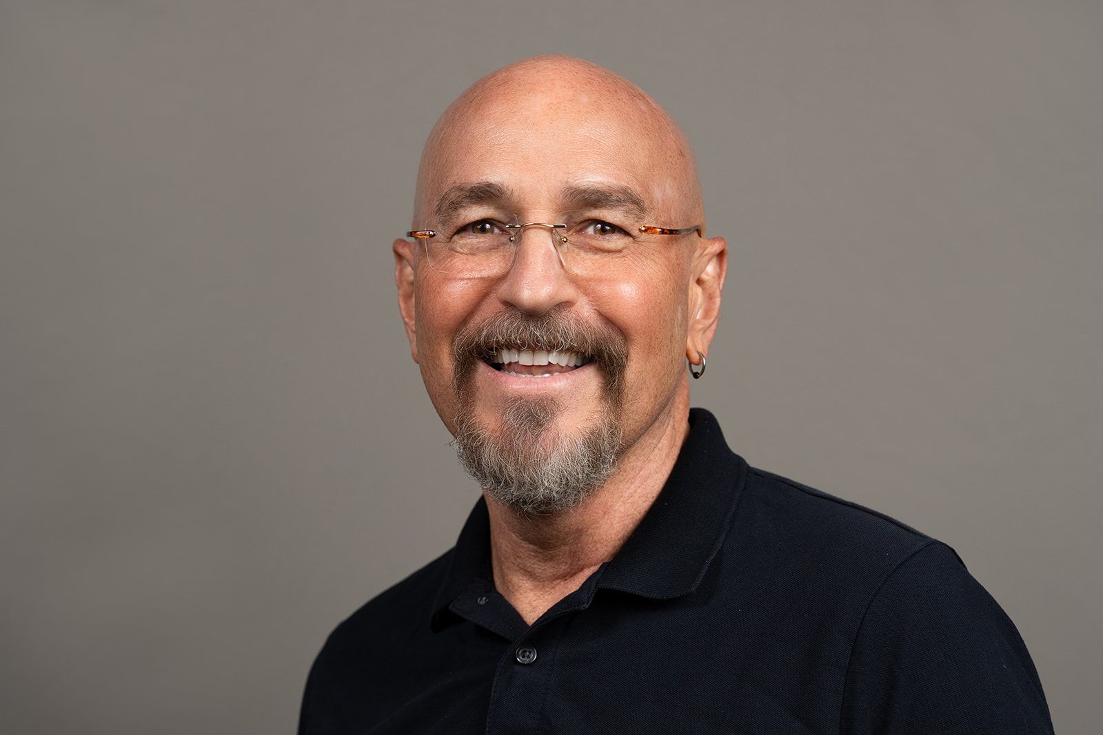 A bald man with a beard and glasses is smiling for the camera.