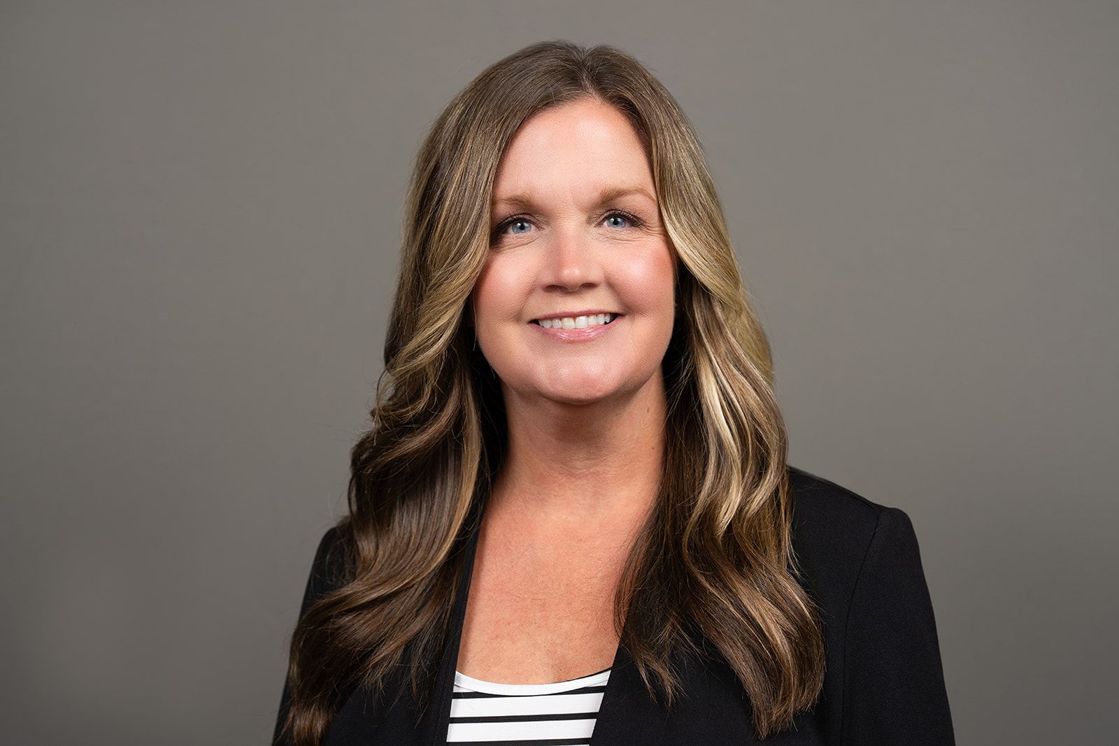 A woman in a black jacket and striped shirt is smiling for the camera.