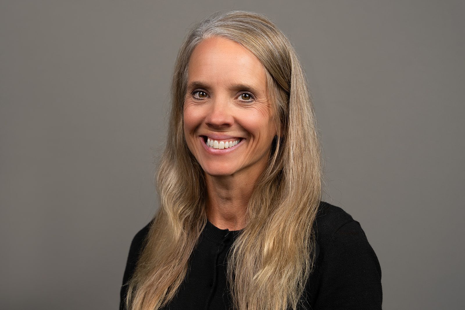 A woman with long blonde hair is smiling and wearing a black shirt.