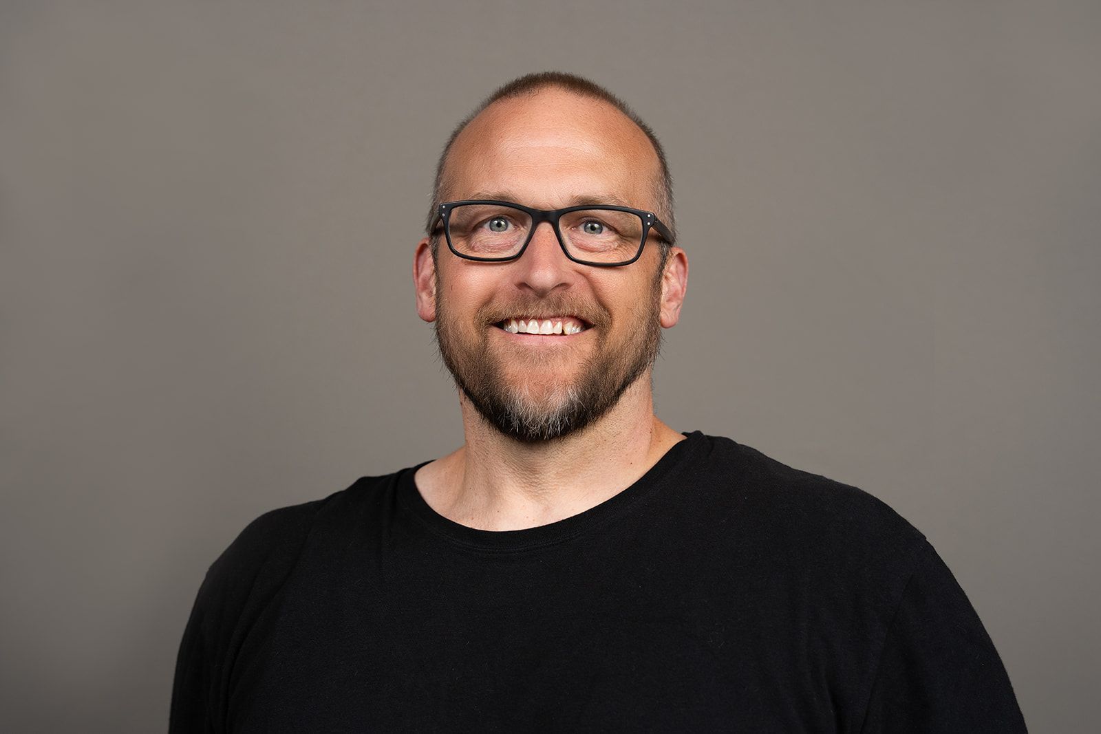 A man wearing glasses and a black shirt is smiling for the camera.