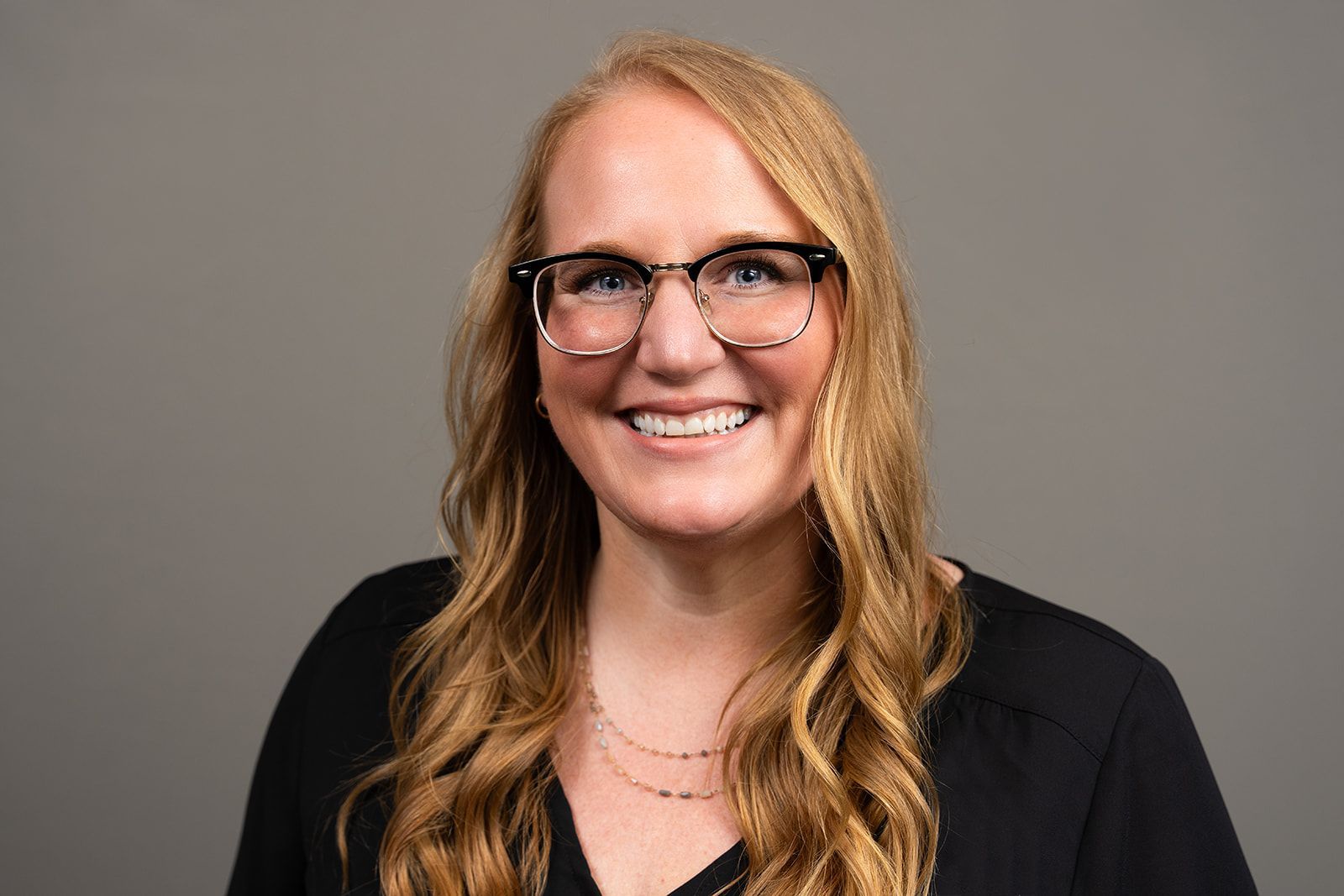 A woman wearing glasses and a black shirt is smiling for the camera.