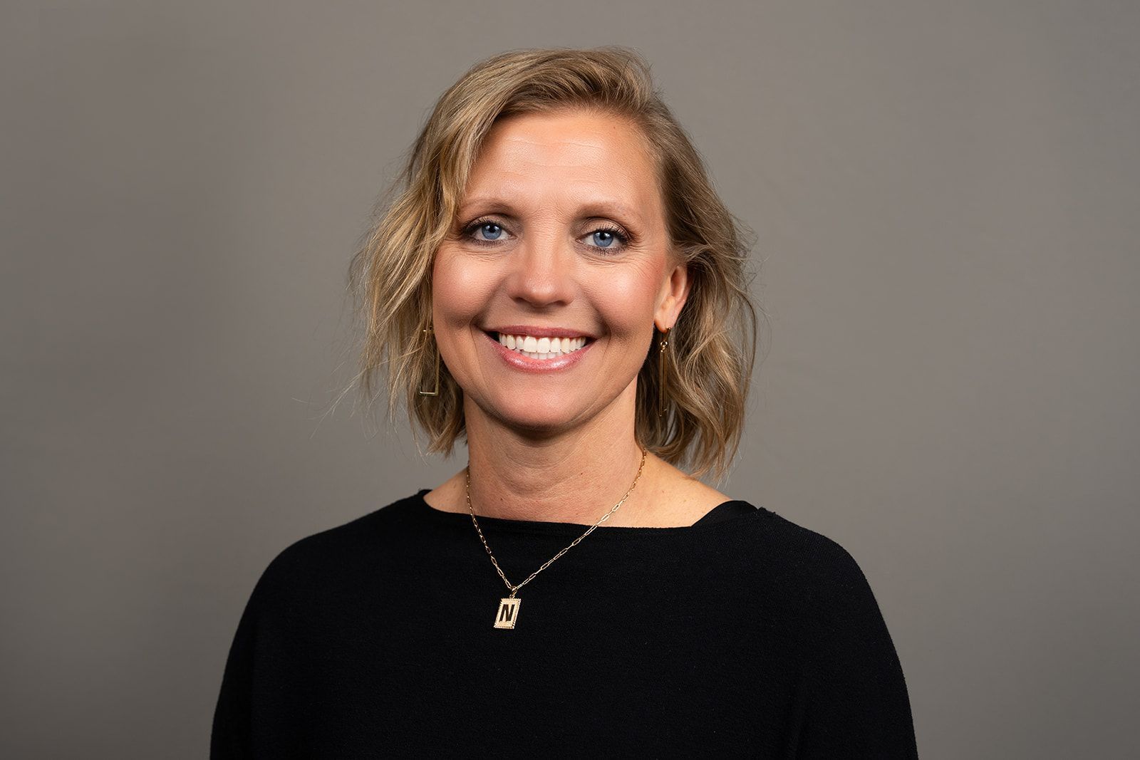 A woman wearing a black shirt and a necklace is smiling for the camera.