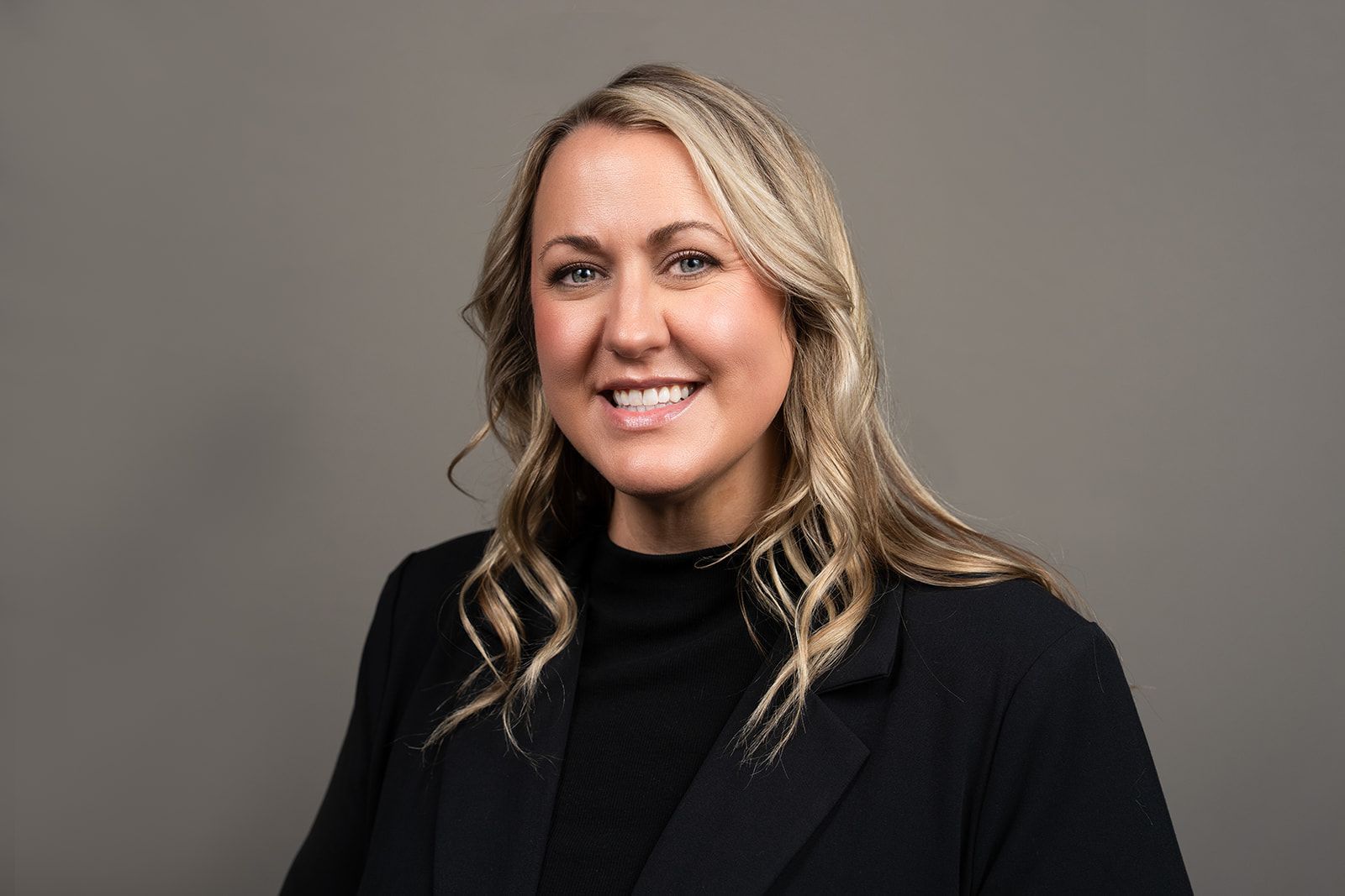 A woman in a black jacket is smiling for the camera.