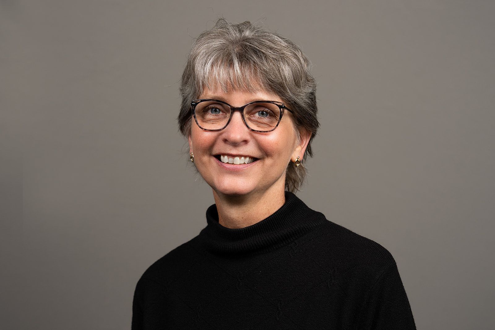 A woman wearing glasses and a black sweater is smiling for the camera.