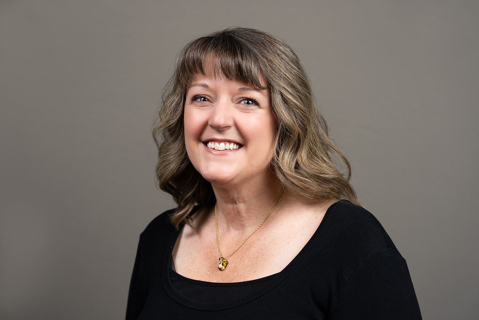 A woman wearing a black shirt and a gold necklace is smiling for the camera.
