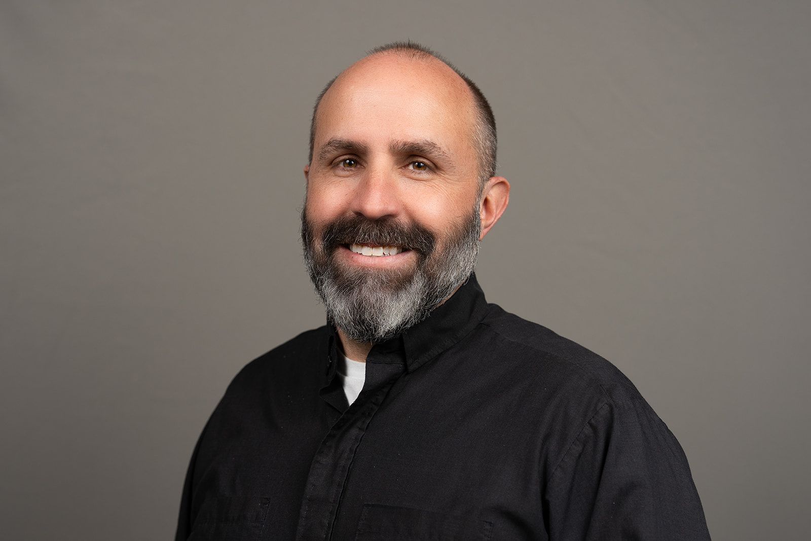 A man with a beard is wearing a black shirt and smiling for the camera.