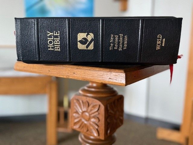 A holy bible is sitting on top of a wooden table.