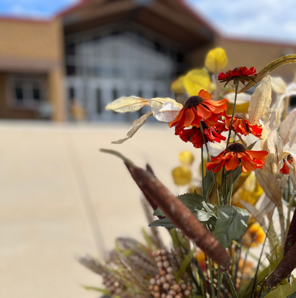 Autumn floral arrangement in front of a school entrance, featuring orange and yellow flowers and a white pumpkin.