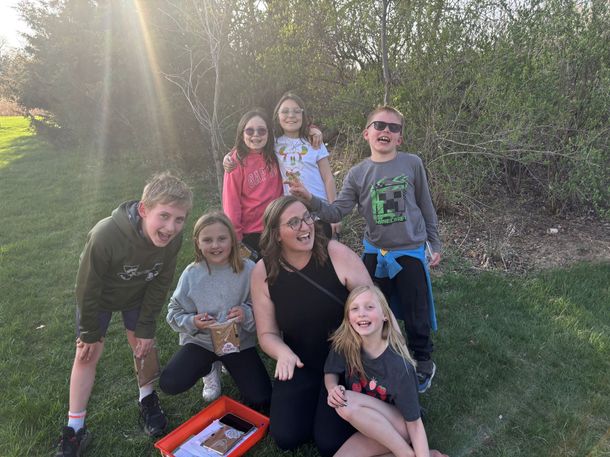 A group of children and a woman are posing for a picture in the grass.