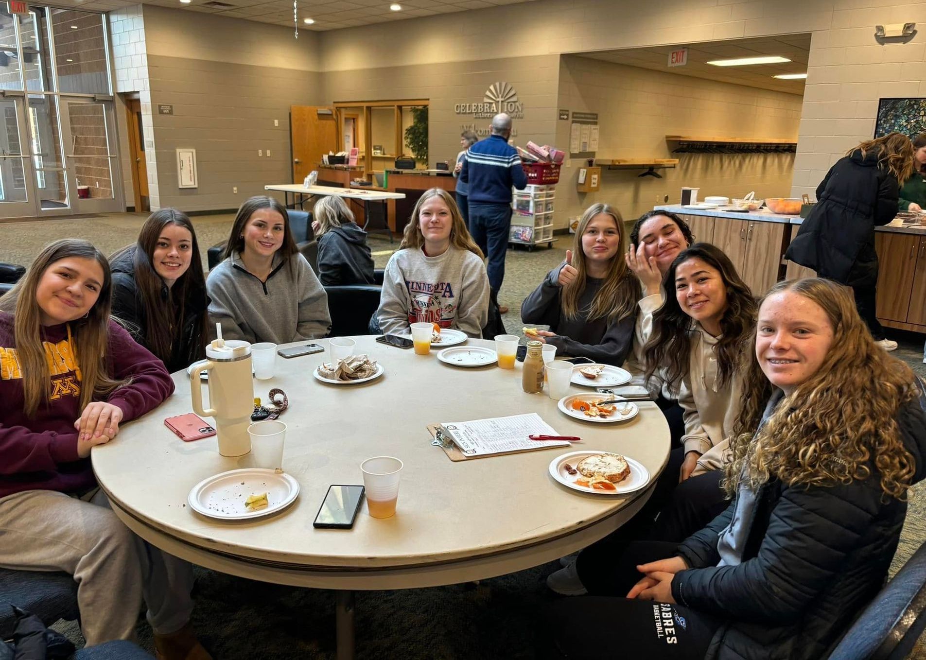A group of young women are sitting around a round table with plates of food.