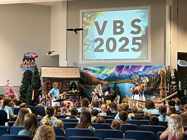 A group of people are sitting in front of a large screen that says vbs 2025.