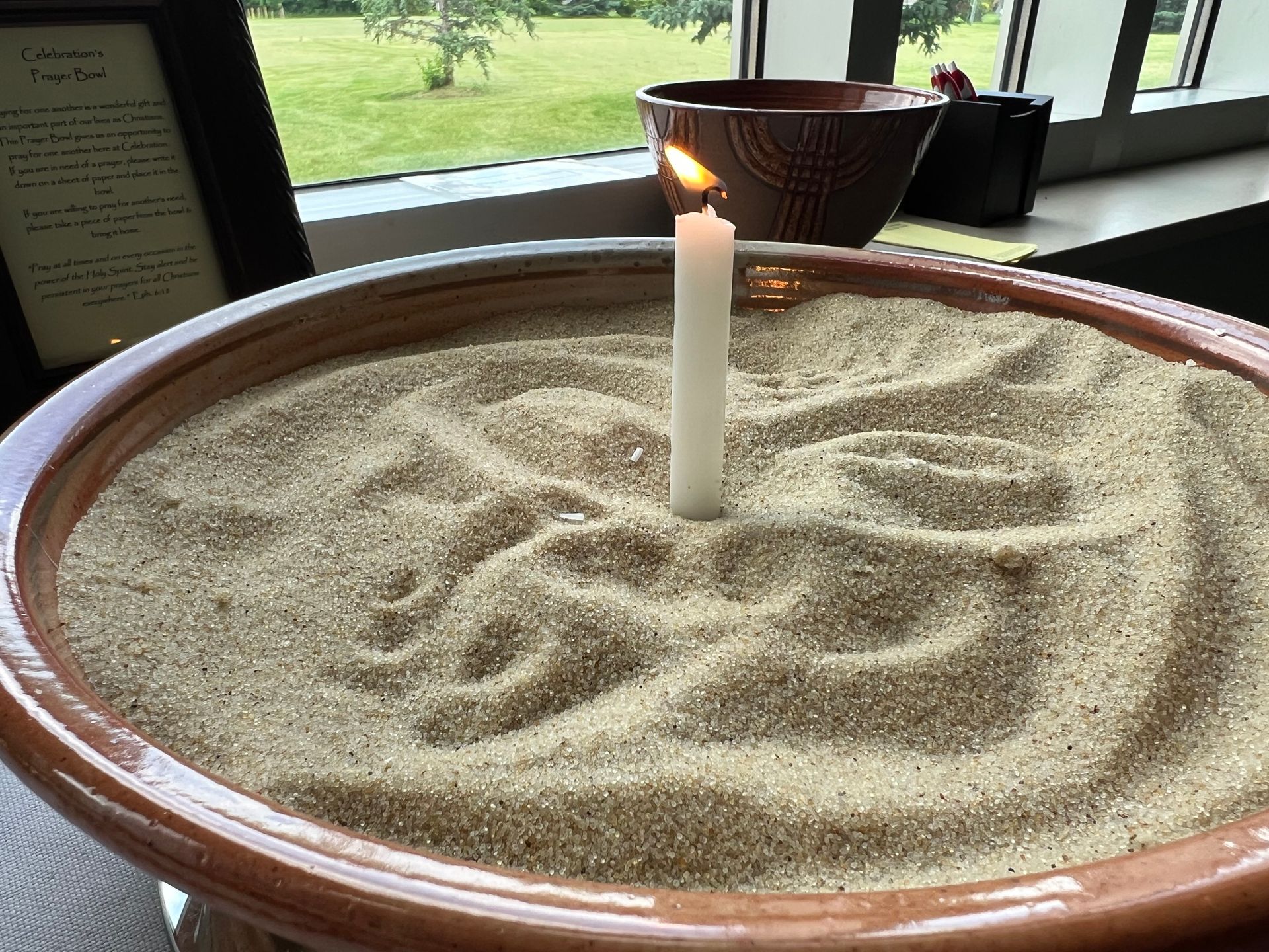 A candle is lit in a bowl of sand