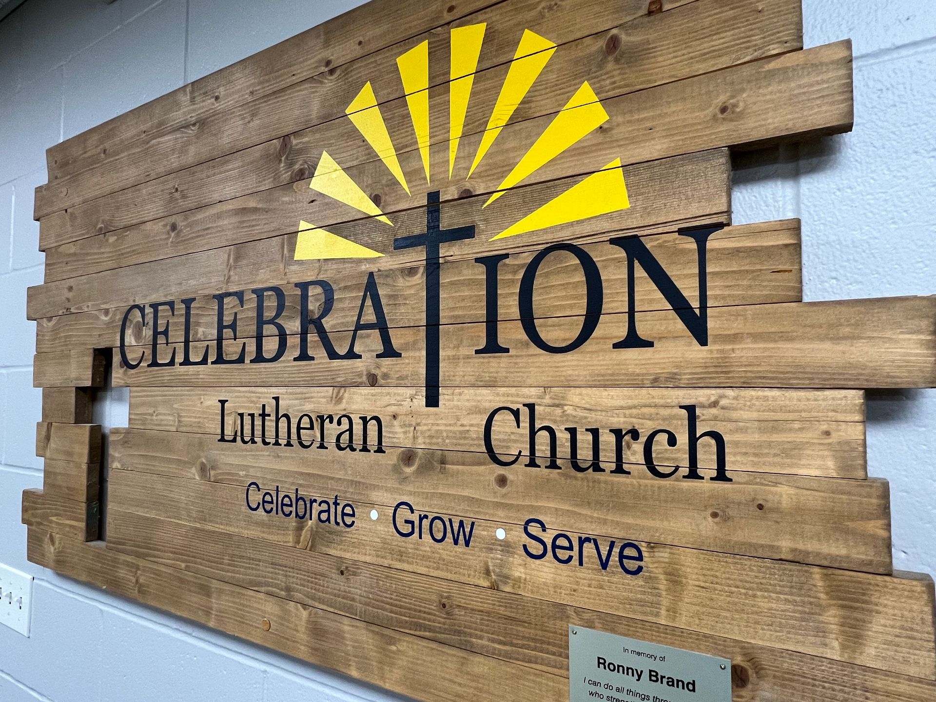 A wooden sign for celebration lutheran church is hanging on a wall.