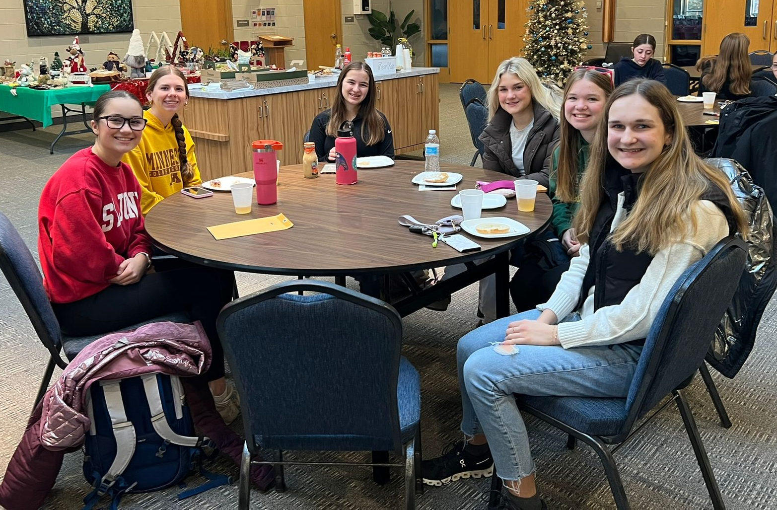 A group of young women are sitting around a round table with plates of food.