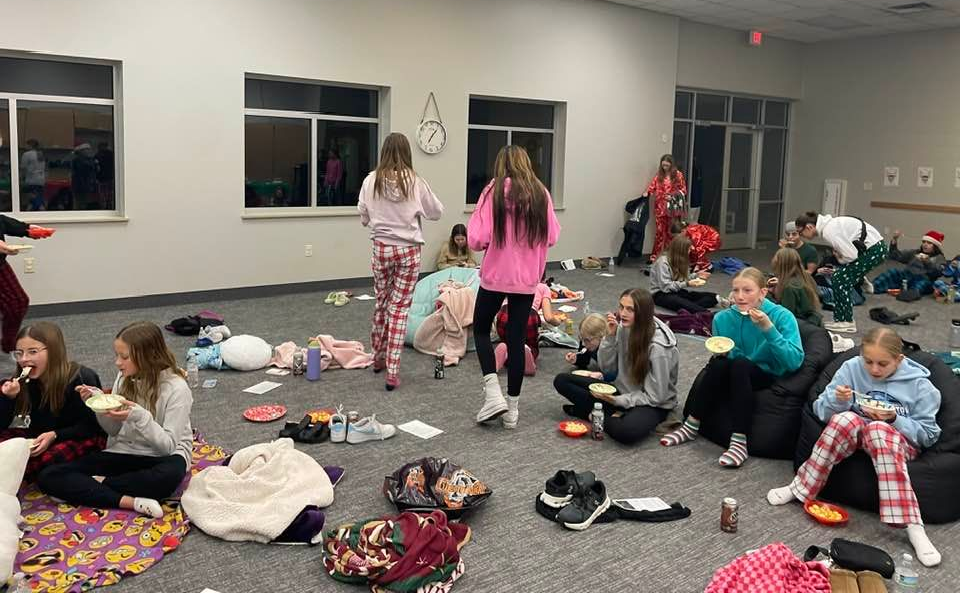 A group of people sitting around a table in a room, interacting and eating.