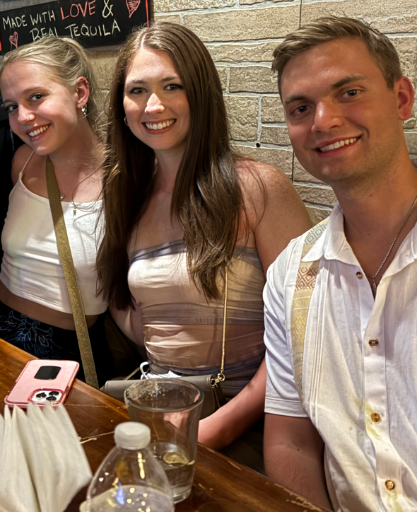 Three people are posing for a picture in front of a sign that says made with love and tequila