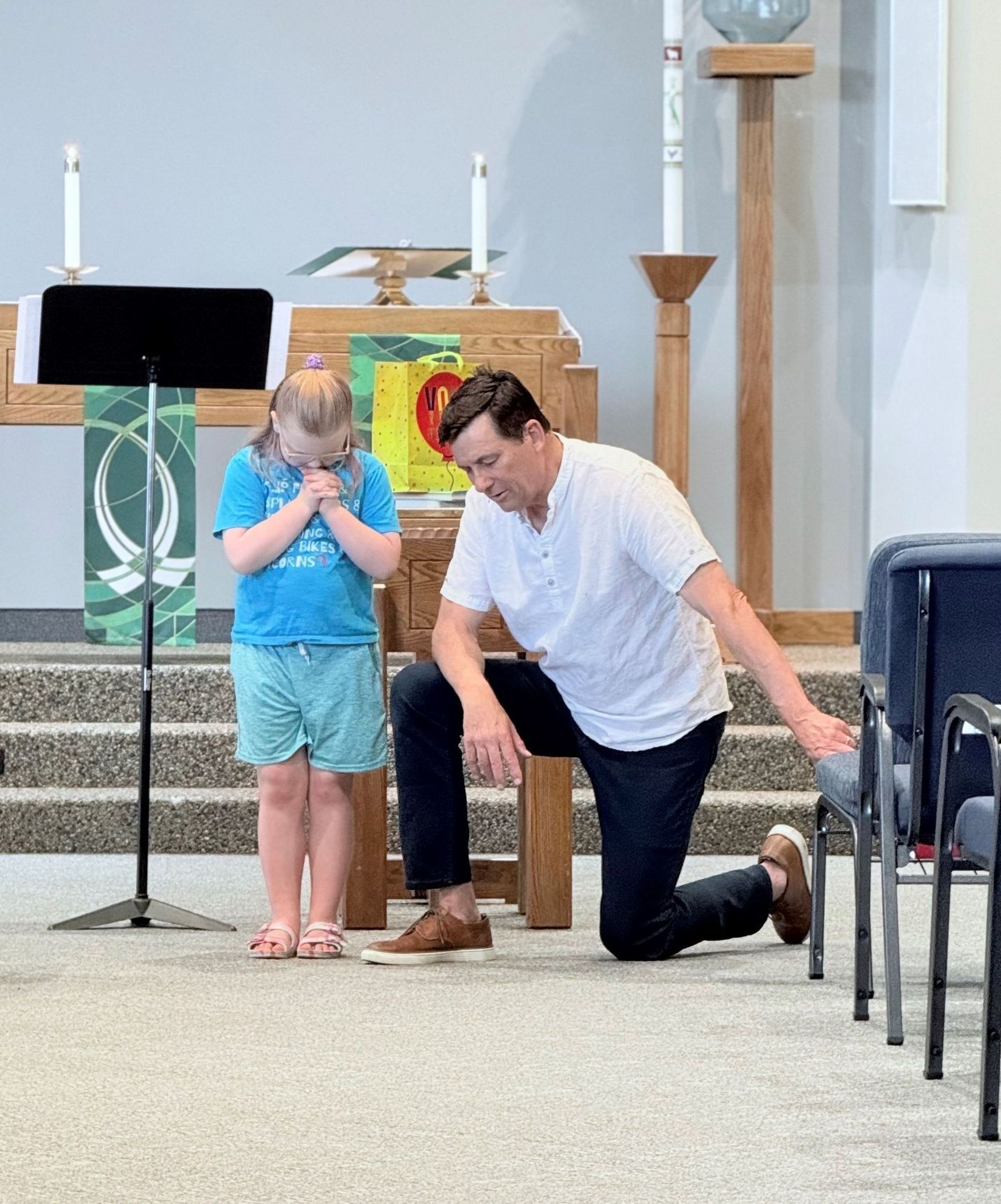A man is kneeling down next to a little girl in a church.