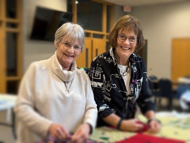 Two women are sitting at a table and smiling for the camera