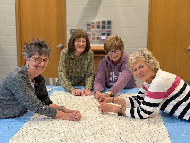 A group of women are sitting around a table making a quilt.