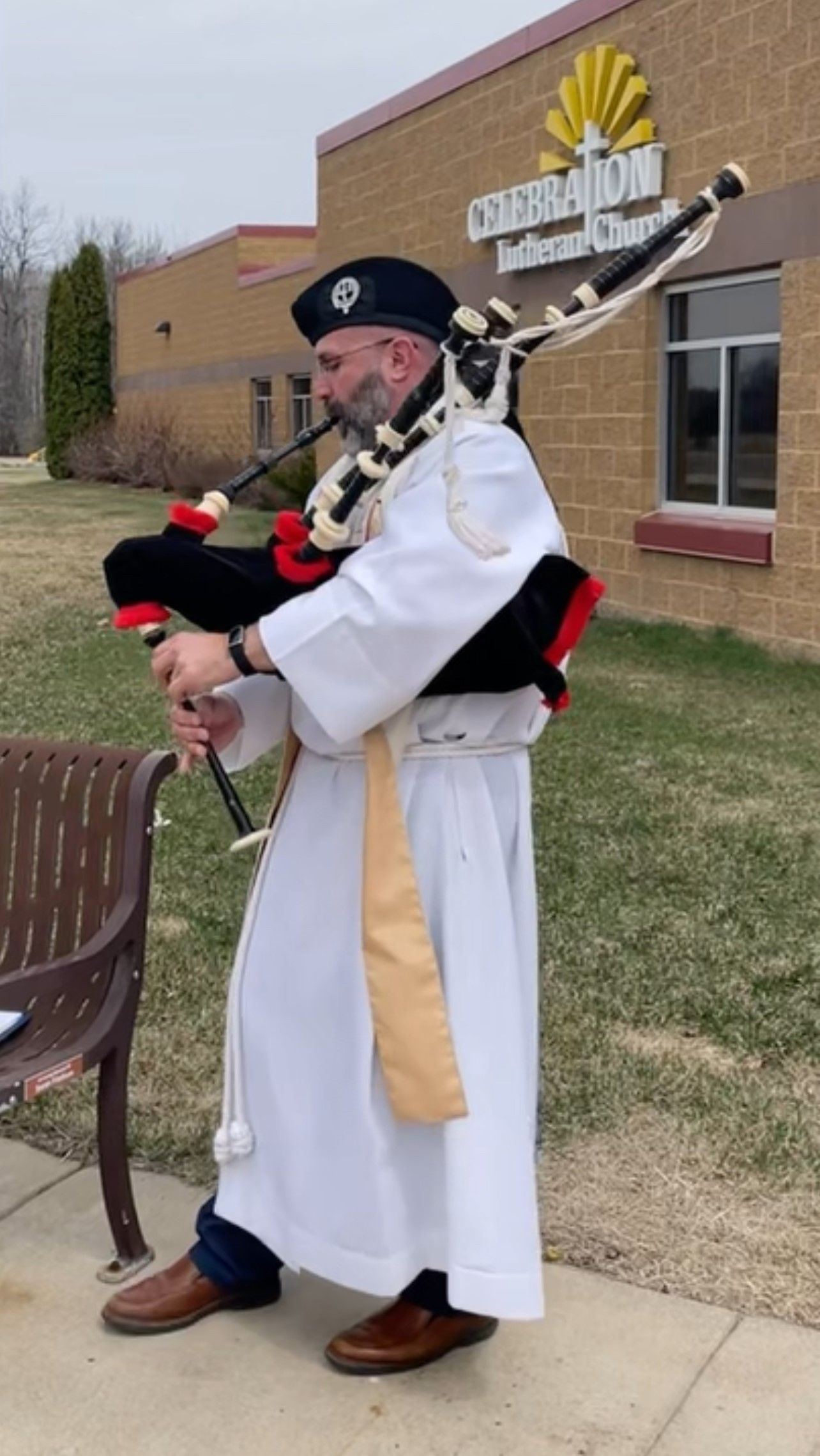 A man in a white robe is playing bagpipes in front of a building