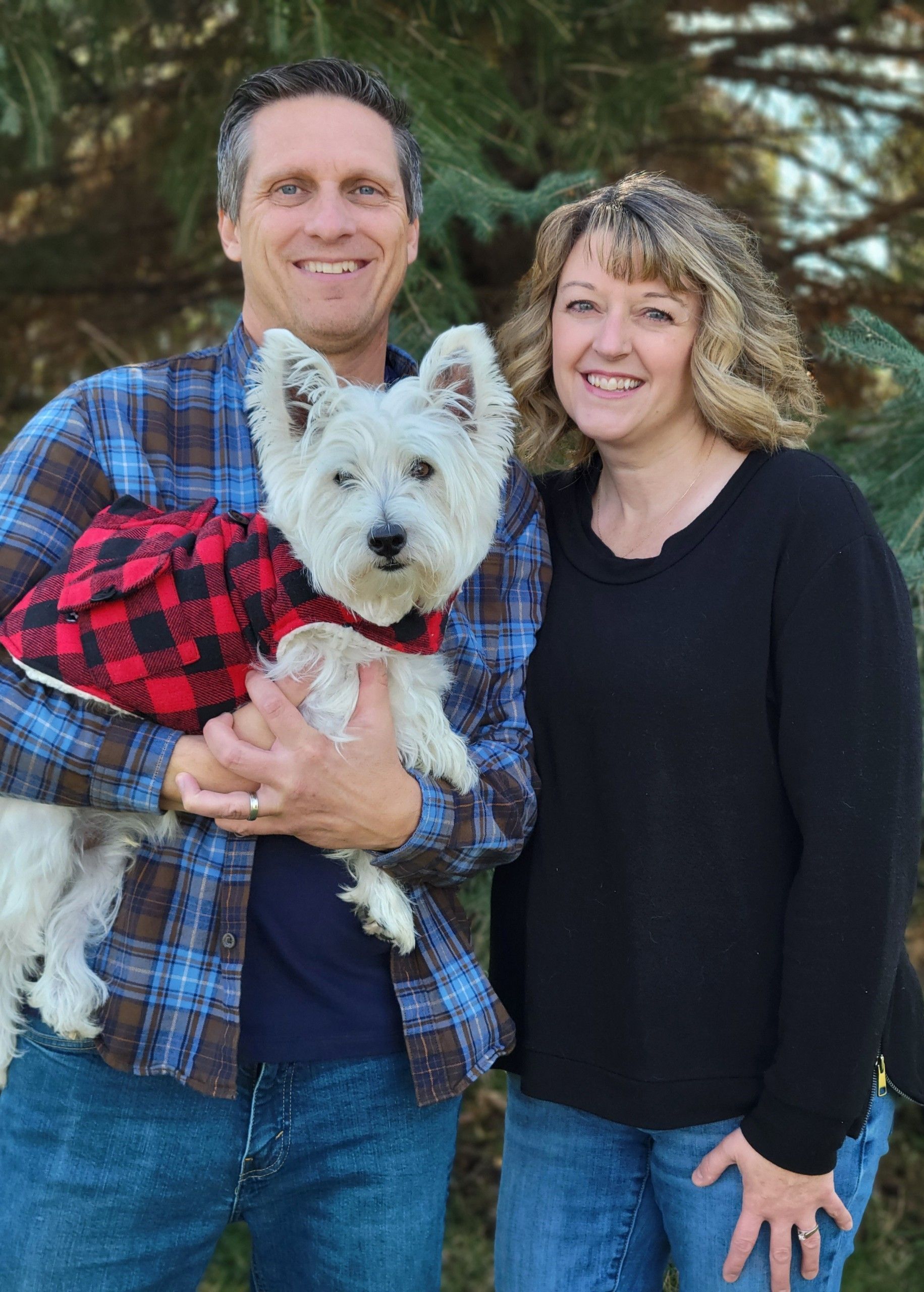 A man and woman are holding a small white dog in their arms.