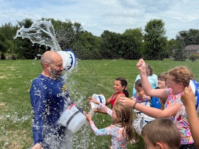 Man being doused with water by laughing children outdoors on a grassy lawn