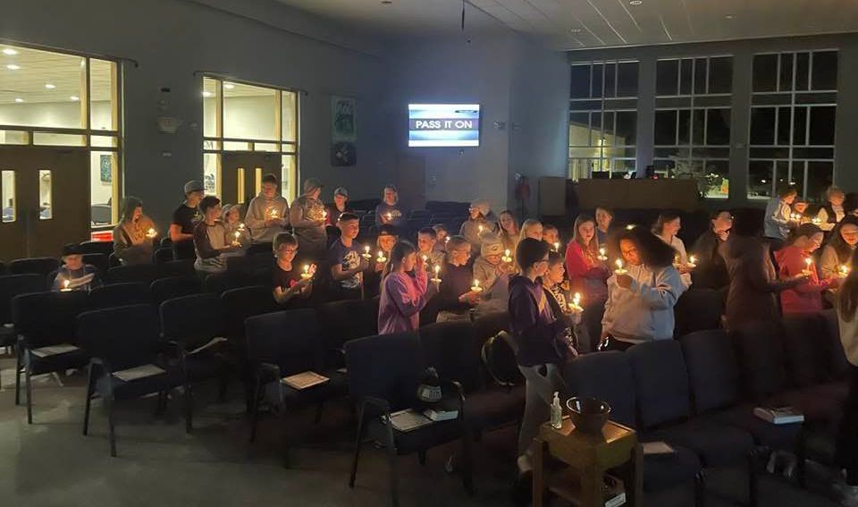 A group of people are sitting in a room holding candles.