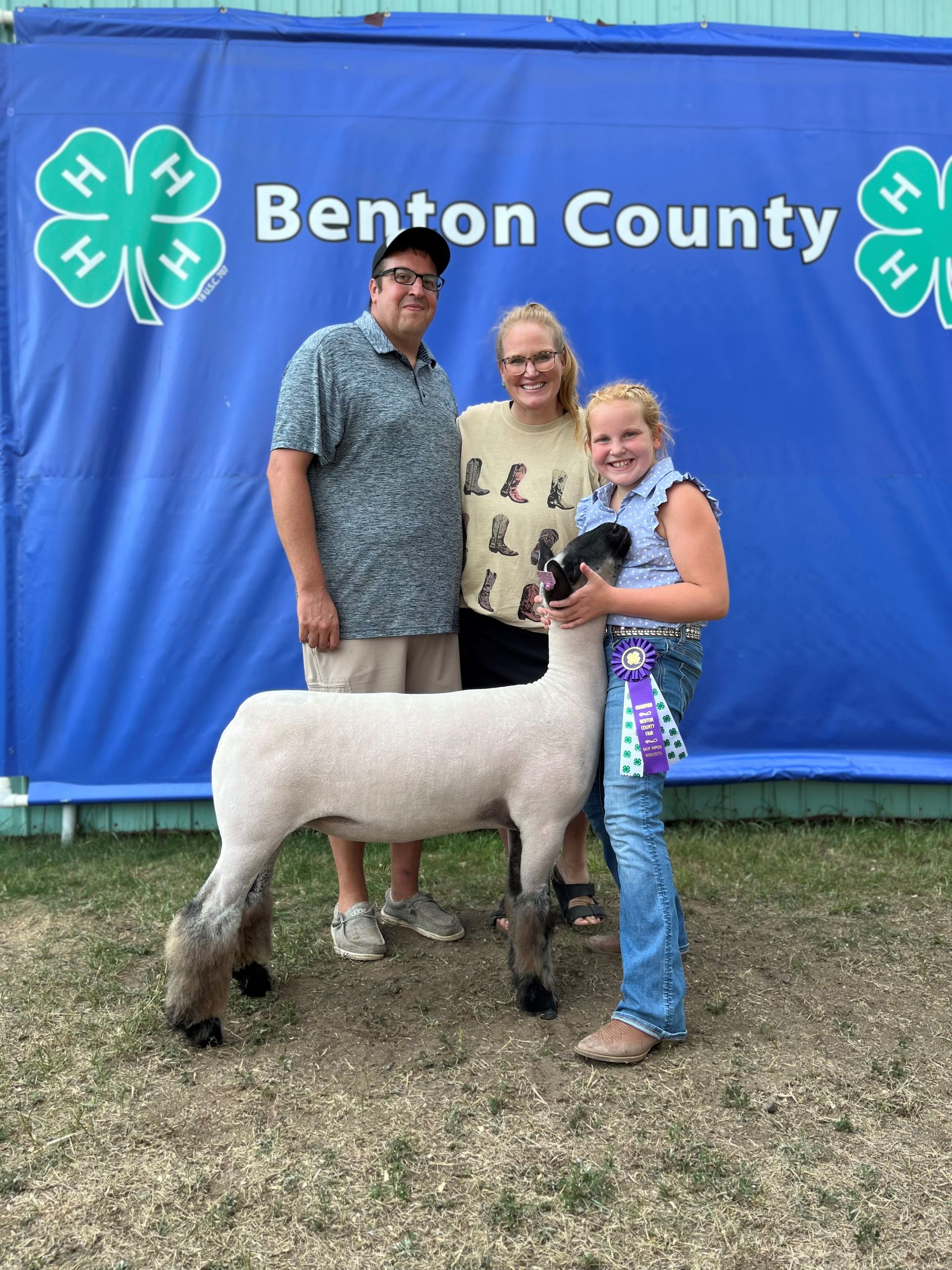 A group of people standing next to a sheep in front of a blue banner that says benton county.