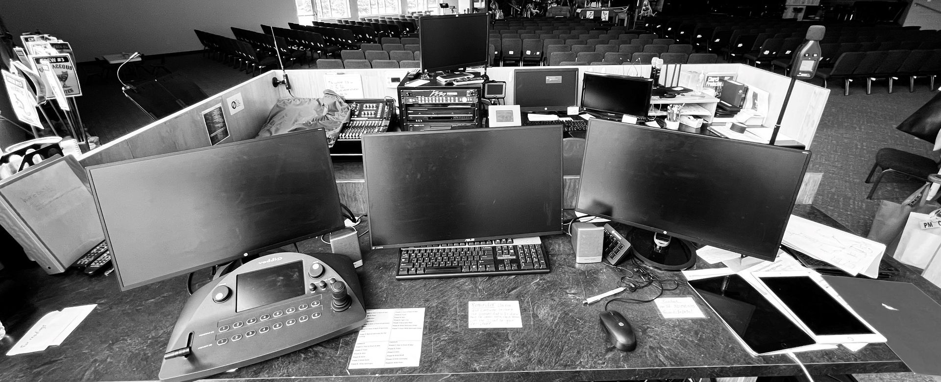 A black and white photo of a desk with computers and a tablet