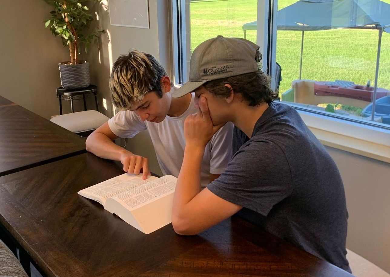 Two boys are sitting at a table reading a book.