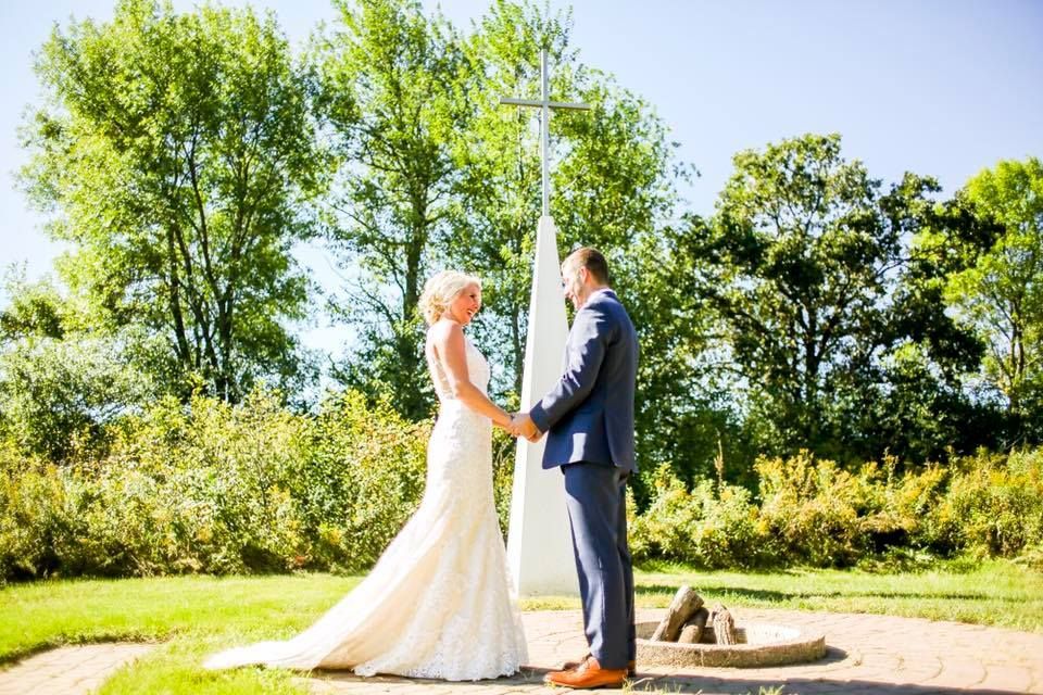 A bride and groom are holding hands in front of a cross.