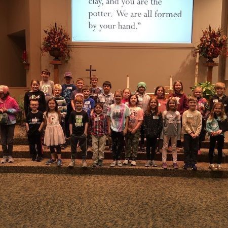 A group of children are posing for a picture in front of a screen that says clay and you are the putter